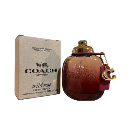 A Coach Wild Rose EDP bottle with a gold-colored cap and a red leather strap, alongside its packaging box.