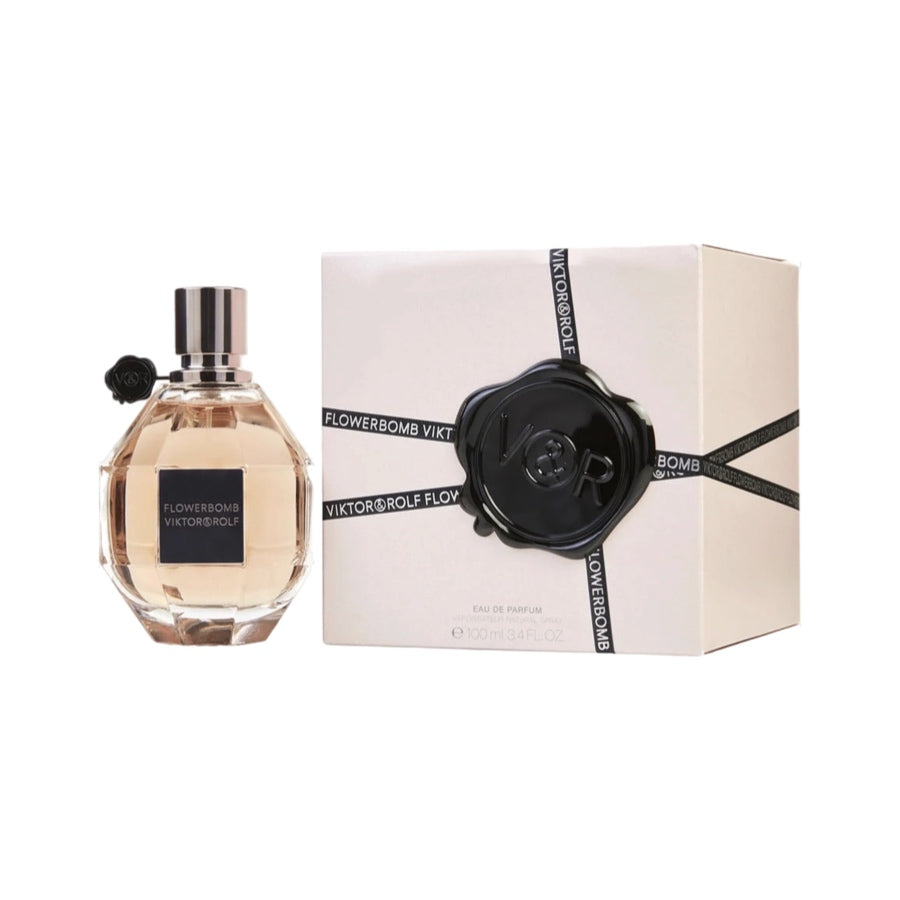 A bottle of Viktor & Rolf Flowerbomb EDP next to its packaging box. The bottle is clear with a black label and spray nozzle, and the box is white with black ribbon details.